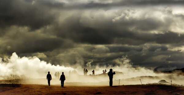 Valley with geothermal springs and geysers. Silhouettes of tourists wandering among clubs a couple erupting from the ground. Geothermal zones a Naumafjal Hverir in the north-eastern part of Iceland.