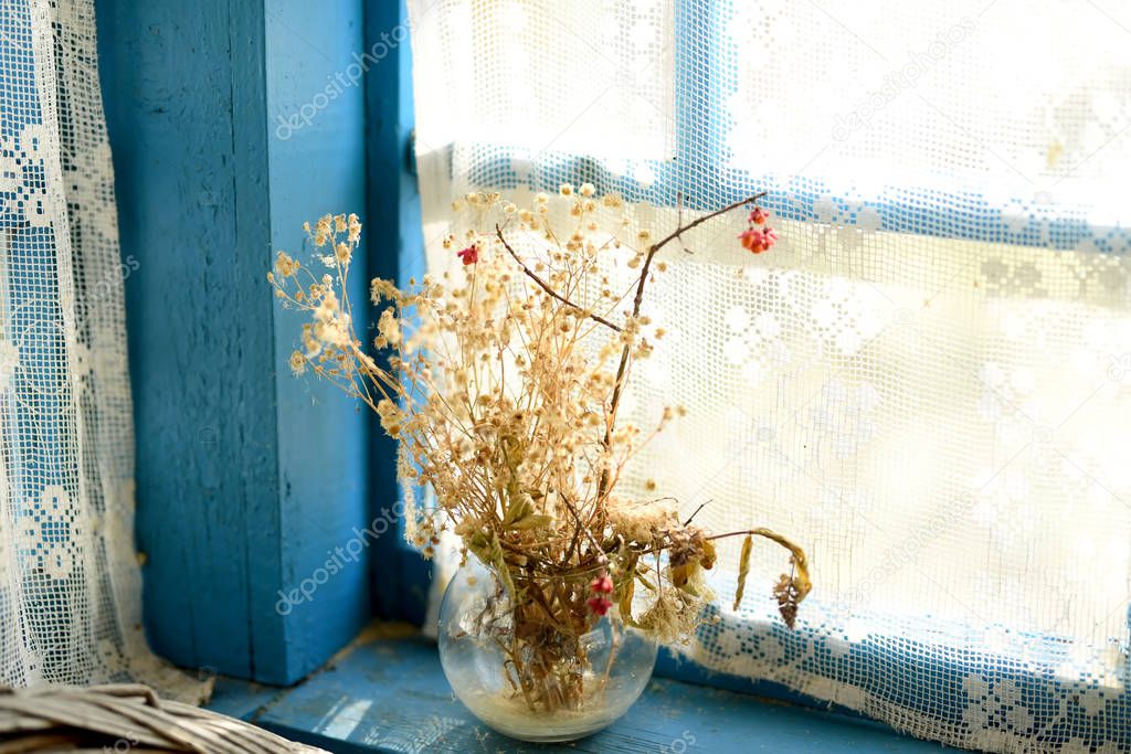 Withered bouquet of wildflowers on an old wooden window of the veranda. Vintage style .