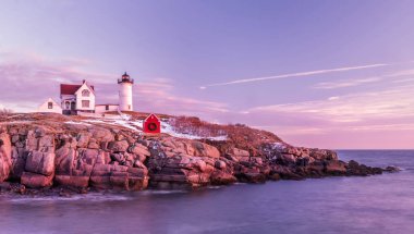 Atlantik Okyanusu kıyısında pembe bulutların olduğu yumuşak bir sabah. Deniz feneri sudaki kayalık bir kayanın üzerinde. Uzun pozlama. Atlantik Okyanusu. Usa. Maine. Nubble York 