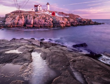 Atlantik Okyanusu kıyısında pembe bulutların olduğu yumuşak bir sabah. Deniz feneri sudaki kayalık bir kayanın üzerinde. Uzun pozlama. Atlantik Okyanusu. Usa. Maine. Nubble York 