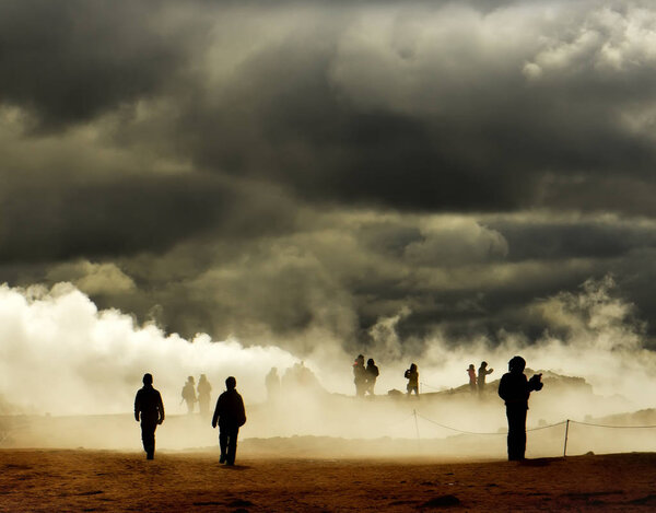 Valley with geothermal springs and geysers. Silhouettes of tourists wandering among clubs a couple erupting from the ground. Geothermal zones a Naumafjal Hverir in the north-eastern part of Iceland.