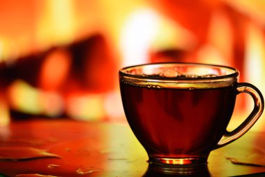 Yanan ateşin arka planında siyah çay olan şeffaf bir fincan. Dinlenme ve rahatlama atmosferi.