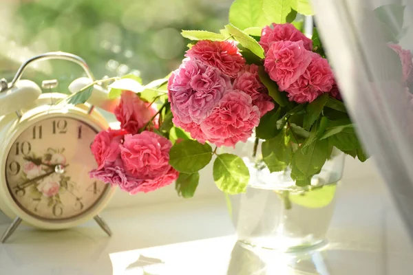 Delicate pink tea roses and a vintage alarm clock on a bright window. Pleasant cute retro vintage still life.