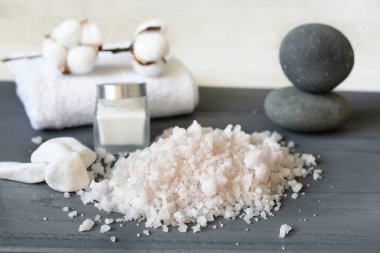 Deniz tuzu kristalleri, gri arka planda bir kavanoz krema ve spa malzemeleri. Rahatlama ve kişisel bakım ortamı.