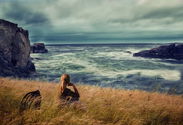 Girl traveler sits on a cliff by the ocean