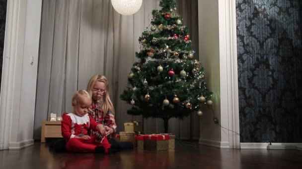 Kleine jongen en meisje openen presenteert op Kerstmis — Stockvideo