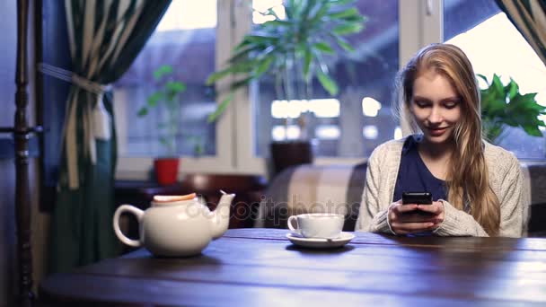 Söpö tyttö kirjoittamalla viestin älypuhelimeen kahvilassa — kuvapankkivideo