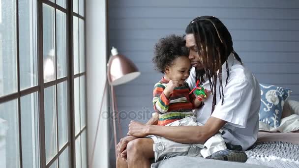 Mieszane rasy chłopiec siedzi na kolanach ojców w domu — Wideo stockowe
