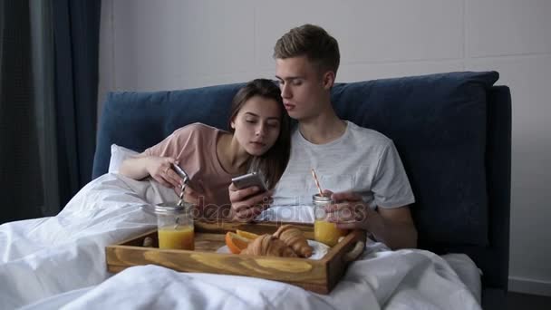 Paar teilt Telefon und schaut Medieninhalte im Bett — Stockvideo