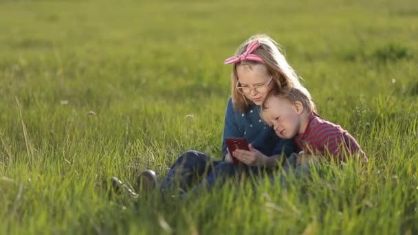 Bambini carini che giocano su smartphone seduti sull'erba . — Video Stock