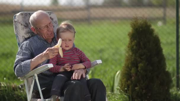 Farfar ger banan till sonsonen utomhus. — Stockvideo
