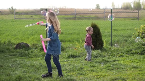 Felices hermanos jugando con burbujas de jabón al aire libre — Vídeos de Stock