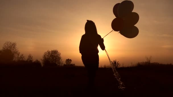 Meisje lopen met ballonnen in veld bij zonsondergang. — Stockvideo