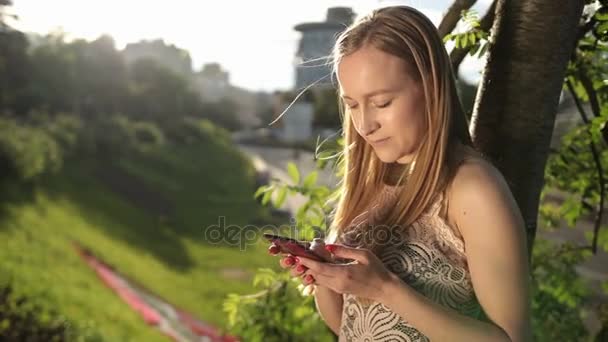 Mujer alegre mensajes de texto en el teléfono inteligente en el parque — Vídeos de Stock