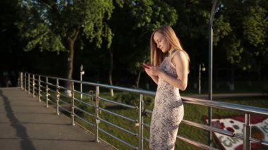 Şık kadın Smartphone köprüde günbatımında kullanarak.