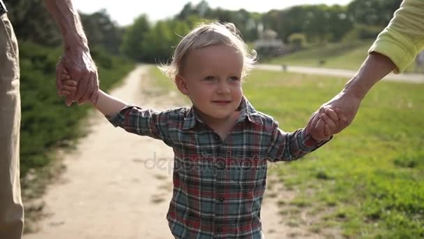 Веселый мальчик, гуляющий с бабушкой и дедушкой в парке — стоковое видео