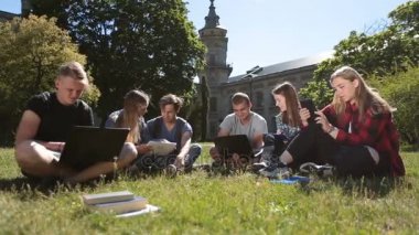 Dizüstü ve tablet ile okuyan öğrenciler çimenlerin üzerinde