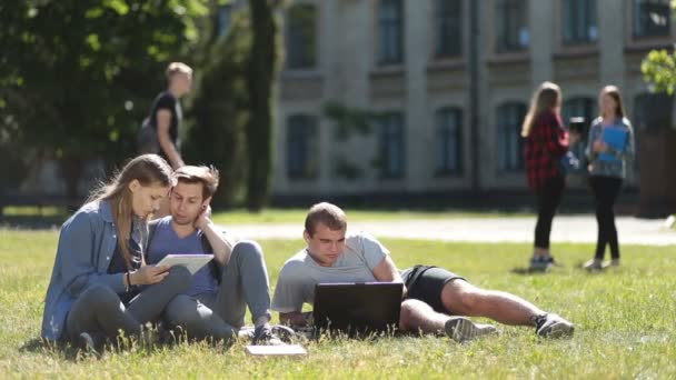 Estudiantes universitarios usando computadora portátil y tableta en el césped — Vídeo de stock