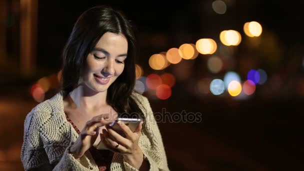 Feliz chica mensaje de texto en el teléfono en la ciudad de la noche — Vídeos de Stock