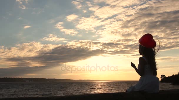 Прекрасна жінка з червоною кулею на морі на заході сонця — стокове відео