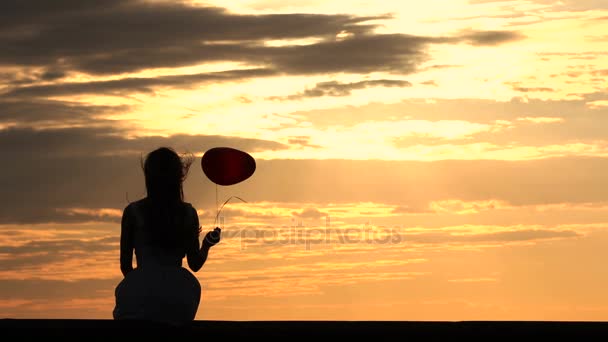 Menina encantadora com balão vermelho desfrutando do pôr do sol — Vídeo de Stock