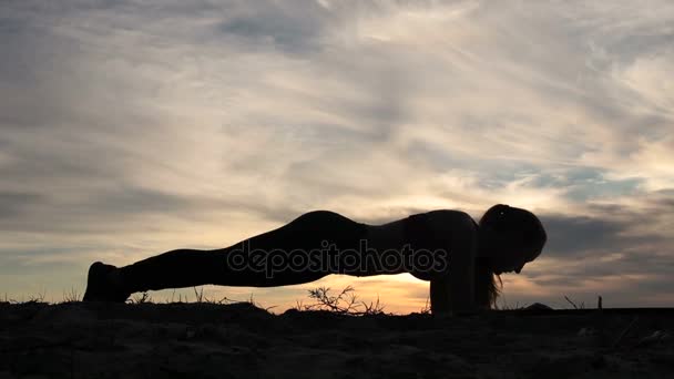 Vrouw doet plank hip wendingen op strand bij zonsondergang — Stockvideo
