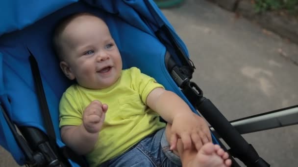 Grappige baby jongetje in baby wandelwagen in park — Stockvideo