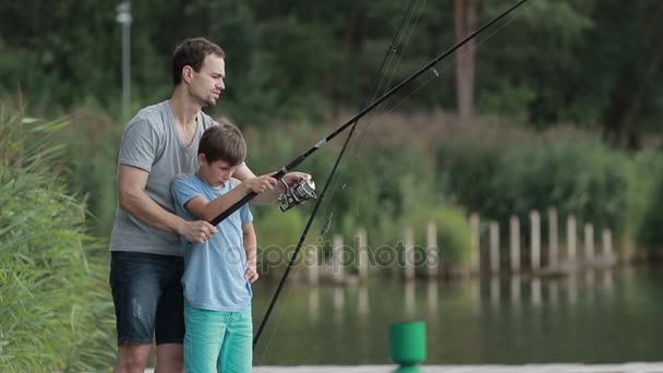 Pai ensinando filho a pescar na margem do lago no verão — Vídeo de Stock