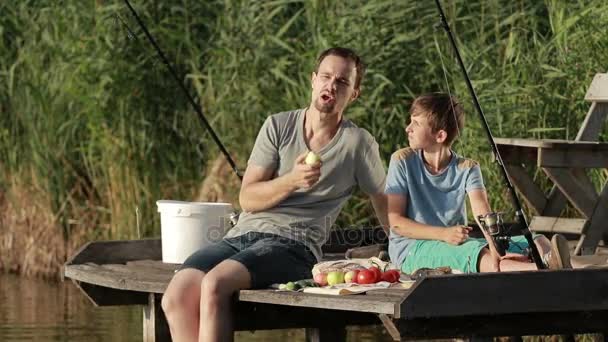 Hipster vader en zoon genietend van picknick bij de vijver — Stockvideo