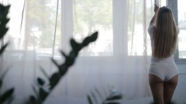 Kadın yatak odasında perdeleri açmayı kusursuz bir beden ile