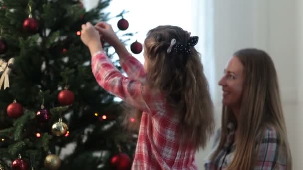 Mädchen hilft ihrer Mutter, den Weihnachtsbaum der Familie zu schmücken — Stockvideo