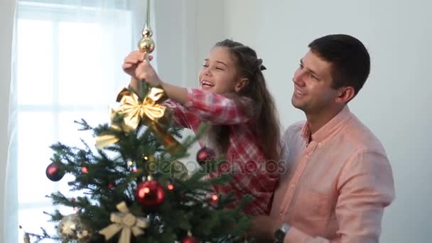 Linda chica poniendo estrella decorativa en la parte superior del árbol de Navidad — Vídeos de Stock