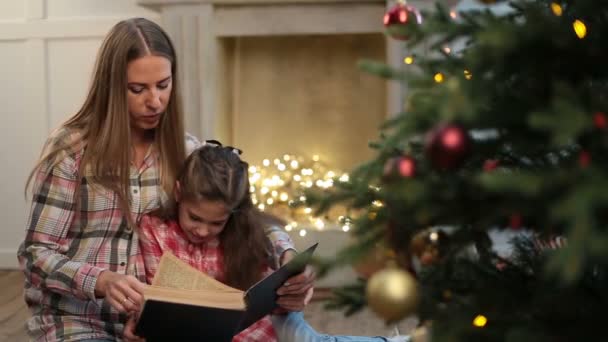 Мать читает книгу дочери возле рождественской елки . — стоковое видео