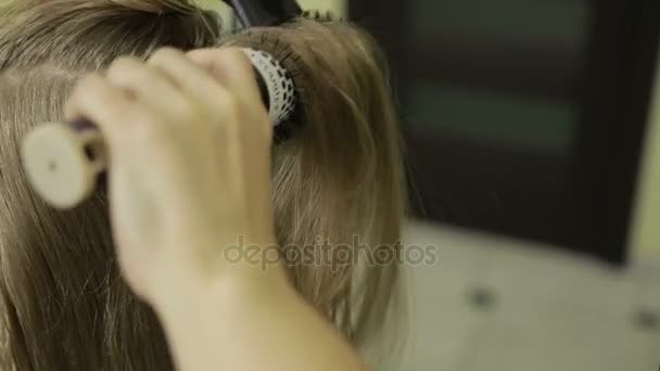 Hairstylist brushing long blonde hair of client