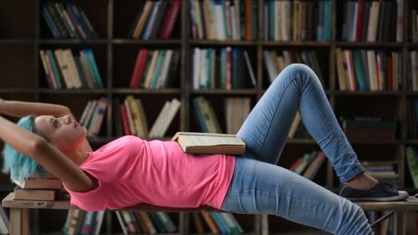 Hipster femenino pensativo leyendo un libro en la biblioteca — Vídeos de Stock