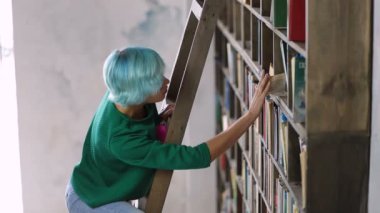 Kız kitap kütüphane içinde arama merdiven üzerinde ayakta