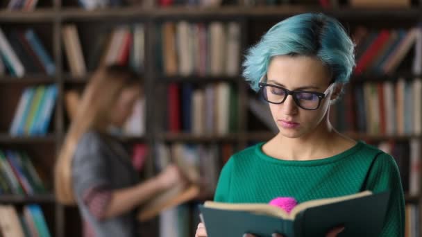 Hipster chica absorto en la lectura de libro en la biblioteca — Vídeo de stock