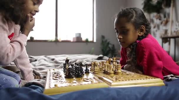 Две умные девочки играют в шахматы на кровати — стоковое видео