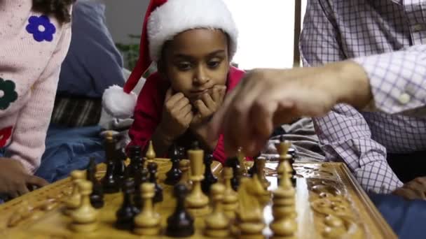 Menina sorridente em santa chapéu assistindo jogo de xadrez — Vídeo de Stock