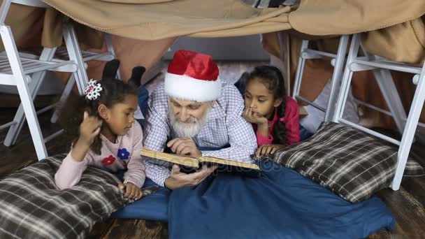 Abuelo en sombrero de santa lectura de un libro con niños — Vídeo de stock