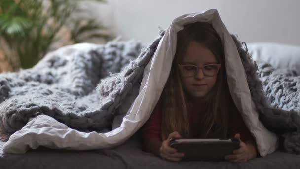 Roztomilá dívka ležící pod deku s touch pad — Stock video