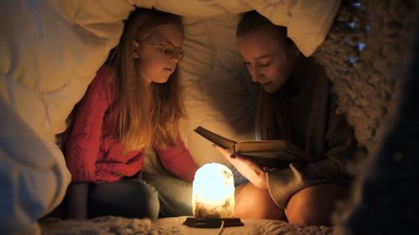 Mamá e hija sentadas debajo de una manta y leyendo — Vídeos de Stock