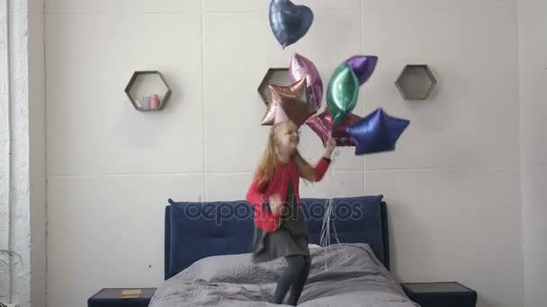 Дівчина-підліток стрибає на ліжку з повітряними кульками на день народження — стокове відео
