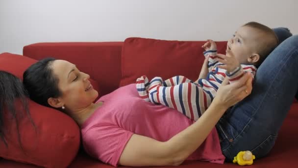 Young mom clapping baby sons hands on couch — Stock Video