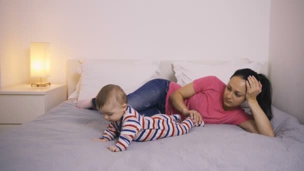 Cansada madre acostada en la cama mirando a su bebé — Vídeos de Stock