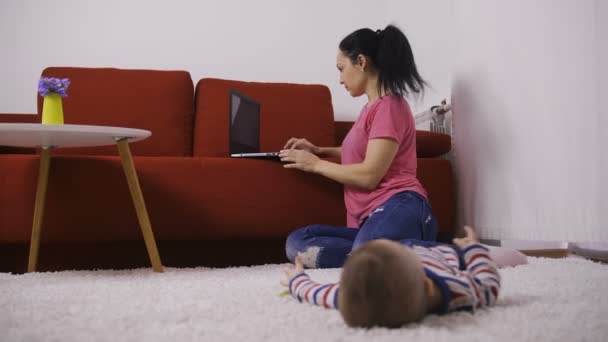 Mother working on laptop near baby son at home — Stock Video