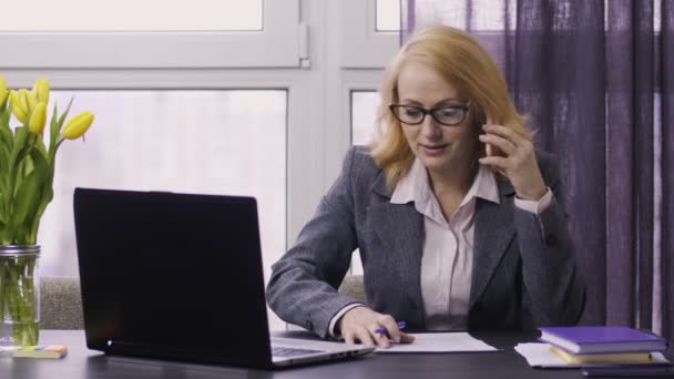 Mujer mayor usando laptop y celular en el trabajo — Vídeos de Stock