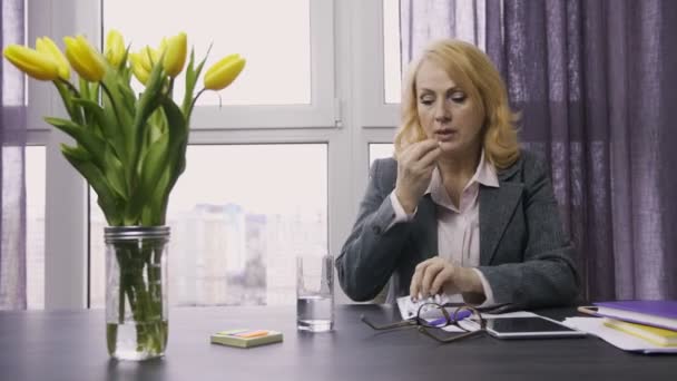 Старшая женщина принимает таблетки от головной боли в офисе — стоковое видео