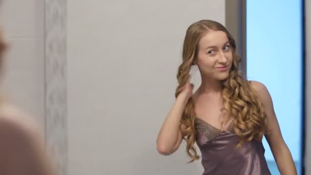 Молодая женщина трогает кудряшки перед зеркалом — стоковое видео