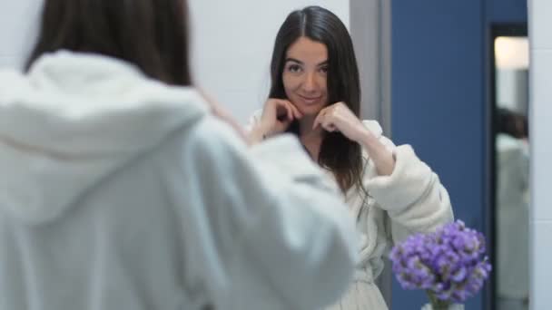 鏡で自分の姿を見ている若い幸せなブルネット — ストック動画
